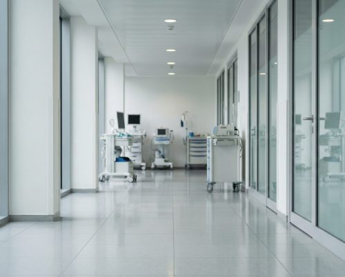 A brightly lit, spotless medical clinic corridor with polished floors, glass partition walls, and mobile medical carts, highlighting professional healthcare facility cleaning, medical office janitorial, and sanitation services.